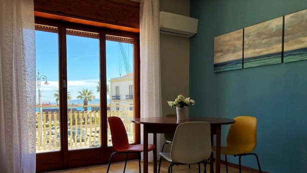 A room with a balcony, a dining table with chairs, and a painting on the wall. - Vacation home IL NIDO (Aeolian Islands boarding) WiFi/park free. CIR 19083049C21 (Milazzo)
