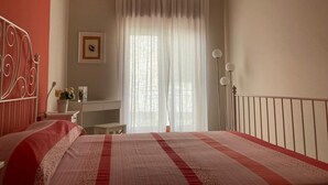 A bedroom with a bed, a desk, a chair, a lamp, and a window with curtains. - Vacation home IL NIDO (Aeolian Islands boarding) WiFi/park free. CIR 19083049C21 (Milazzo)