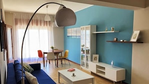 A living room with a blue sofa, a white coffee table, and a dining area with a table and chairs. - Vacation home IL NIDO (Aeolian Islands boarding) WiFi/park free. CIR 19083049C21 (Milazzo)
