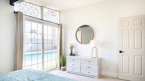 Quarto com uma janela grande, uma cama, penteadeira, espelho e porta.