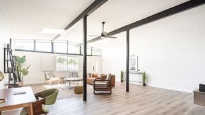 Uma sala de estar ampla, com teto alto, vigas aparentes e uma grande janela que proporciona luz natural.