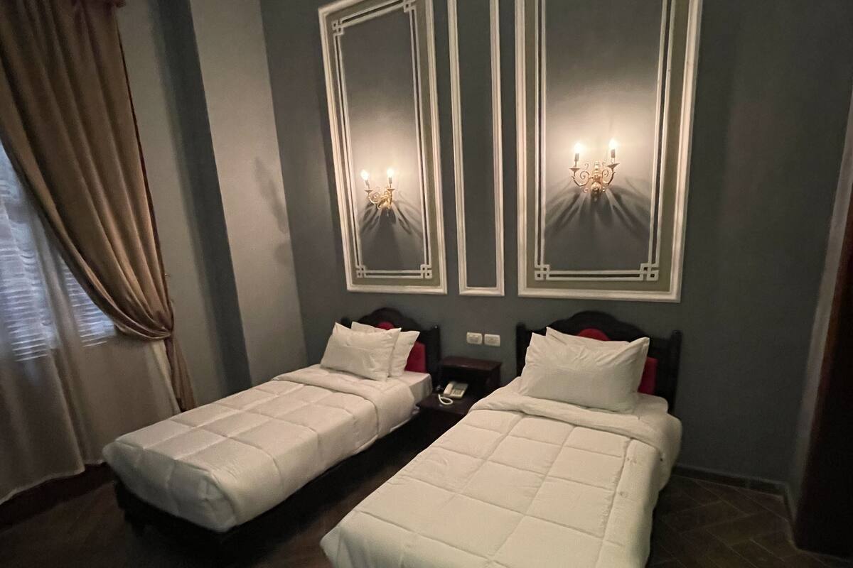A hotel room with two beds, a nightstand, a telephone, and a window with curtains.