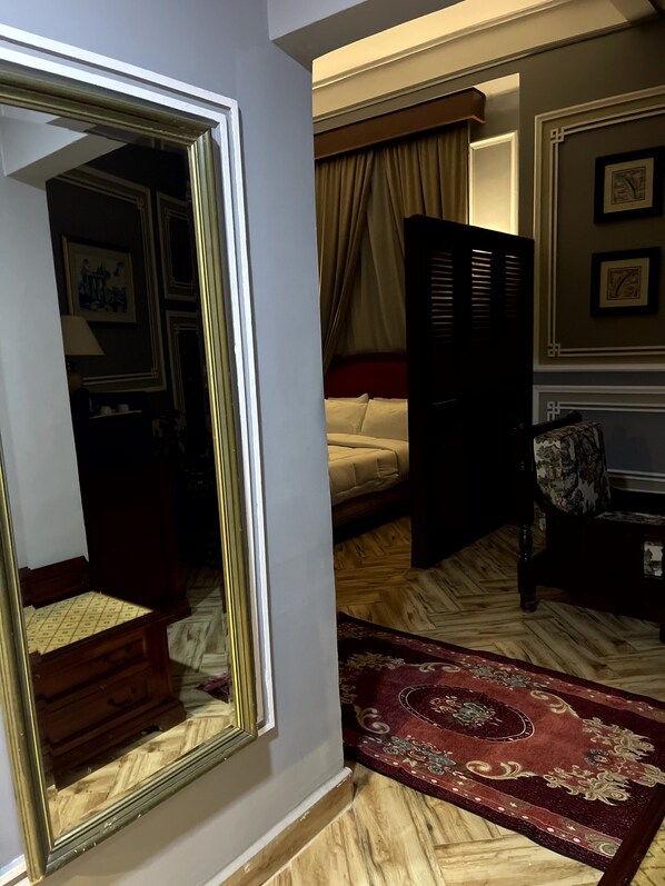Une pièce avec un lit, une chaise, un miroir et un plancher en bois.