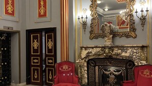 Een statige kamer met een grote, versierde spiegel, rode fauteuils en een marmeren vloer.