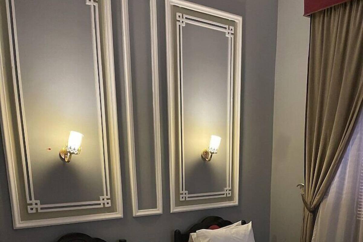 A hotel room with two beds, a dark wooden headboard, a light-colored floor, and wall-mounted sconces.