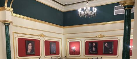 A formal dining area with tables set for four, ornate chairs, and framed portraits on the walls.