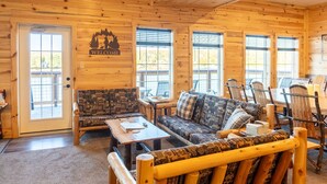A log cabin interior with a wooden door, a welcome sign, a sofa, a table, and a dining area with chairs. - Waterfront Trailside Cabin 23B (Houghton)