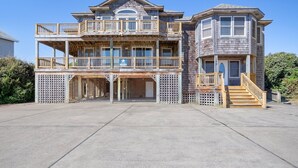 A two-story wooden house with a balcony, a porch, and a staircase leading to the upper level. - Happy Days: 2-Min Walk Beach, Pool, Hot Tub, 7BR (Southern Shores)