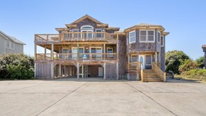 A multi-story wooden house with a balcony, a porch, and a staircase leading to the upper levels. - Happy Days: 2-Min Walk Beach, Pool, Hot Tub, 7BR (Southern Shores)