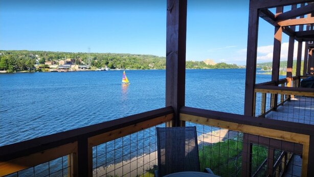 A lakeside view from a wooden deck with a sailboat in the distance.