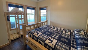 A bedroom with a bunk bed, large windows with a view of the sea, and a checkered bedspread.