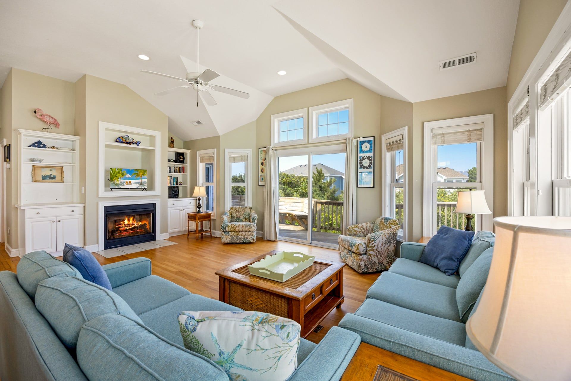 A spacious living room with a fireplace, a ceiling fan, and a large window offering a view of the outdoors.