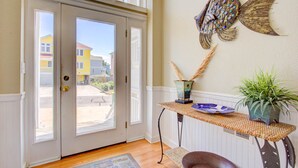 Una habitación con un gran mural de peces, una mesa de mimbre con adornos, y vista a una zona residencial a través de una puerta de vidrio.