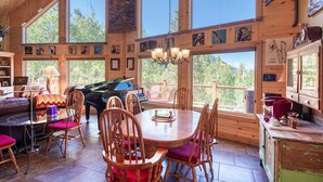 Un interior espacioso de madera con comedor, piano y grandes ventanas que ofrecen vistas al exterior.