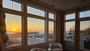 Una habitación con ventanas amplias, vista al atardecer sobre la playa, una silla y una mesita.