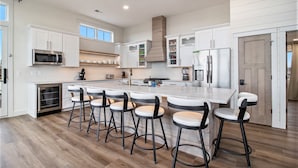 Una cocina moderna con armarios blancos, una isla central con taburetes de bar, electrodomésticos de acero inoxidable y una estufa a leña.