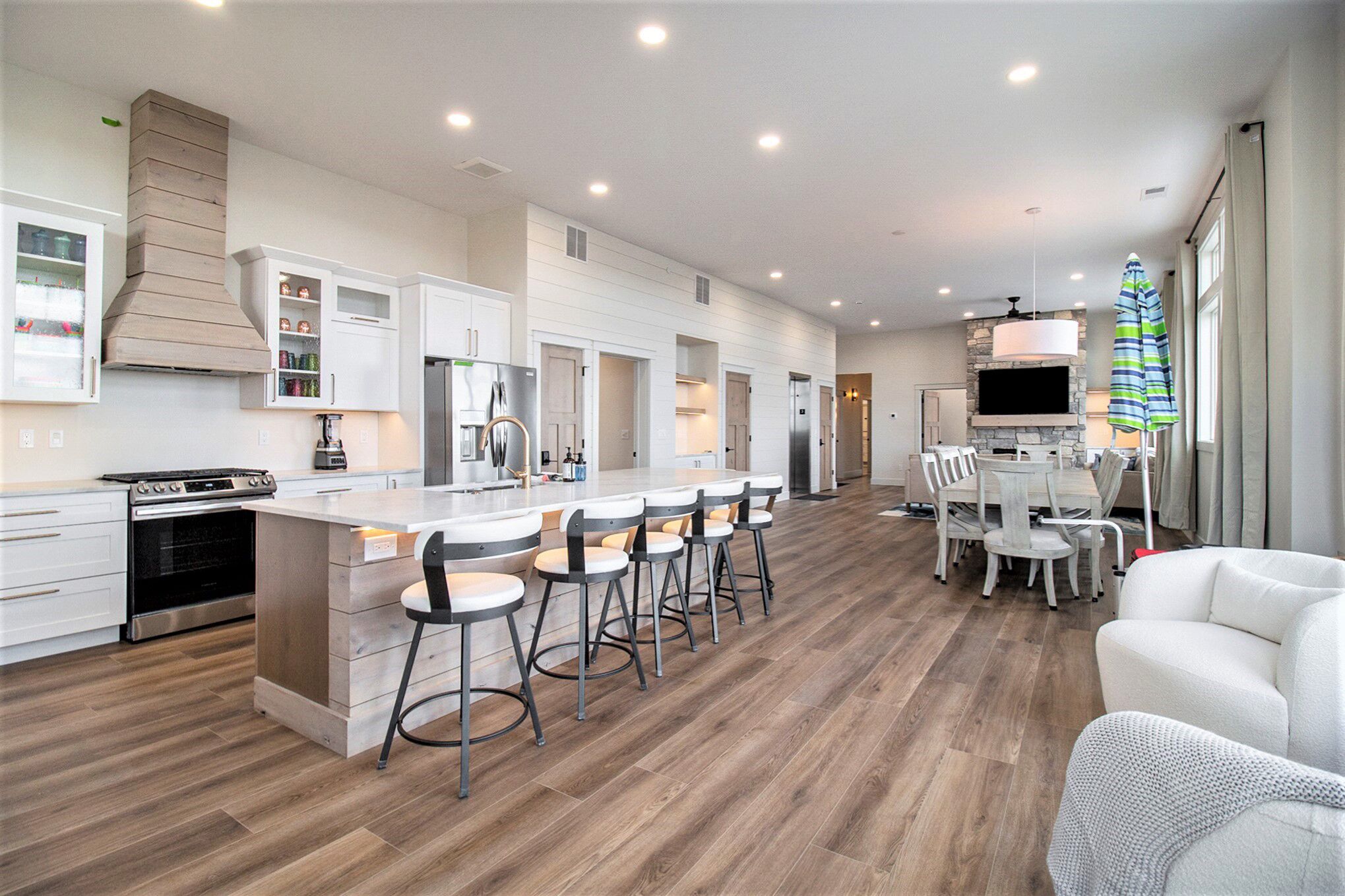 A modern kitchen with a central island, bar stools, a dining area with a table and chairs, and a TV mounted on the wall.