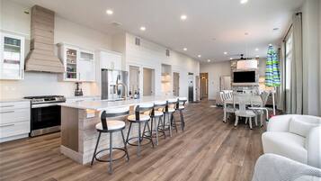 A modern kitchen with a central island, bar stools, a dining area with a table and chairs, and a TV mounted on the wall.
