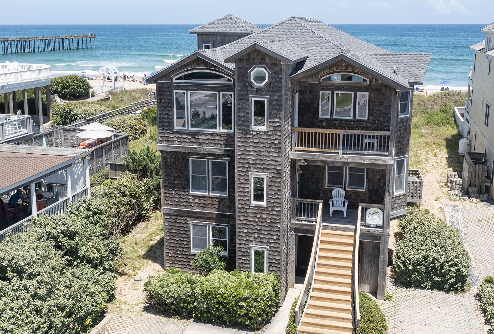 A multi-story wooden building with balconies, a wooden staircase, and a beach view.