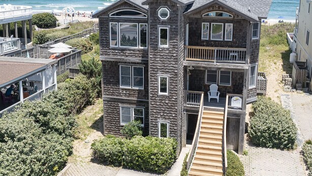 A multi-story wooden building with balconies, a wooden staircase, and a beach view. - 6067 The Sand Pebble *Pool *Game Rm *Dog Friendly (Nags Head)