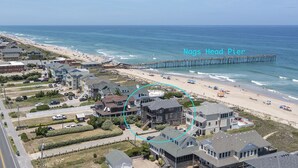 A coastal residential area with a pier extending into the ocean, houses with various architectural styles, and a clear view of the beach. - 6067 The Sand Pebble *Pool *Game Rm *Dog Friendly (Nags Head)