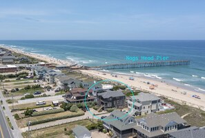 A coastal residential area with a pier extending into the ocean, houses with various architectural styles, and a clear view of the beach. - 6067 The Sand Pebble *Pool *Game Rm *Dog Friendly (Nags Head)