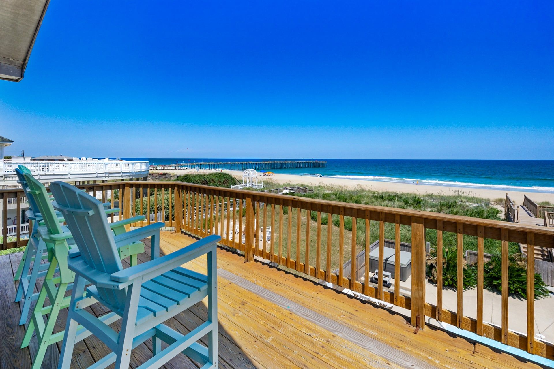 A wooden deck with chairs overlooking a beach and a pier.