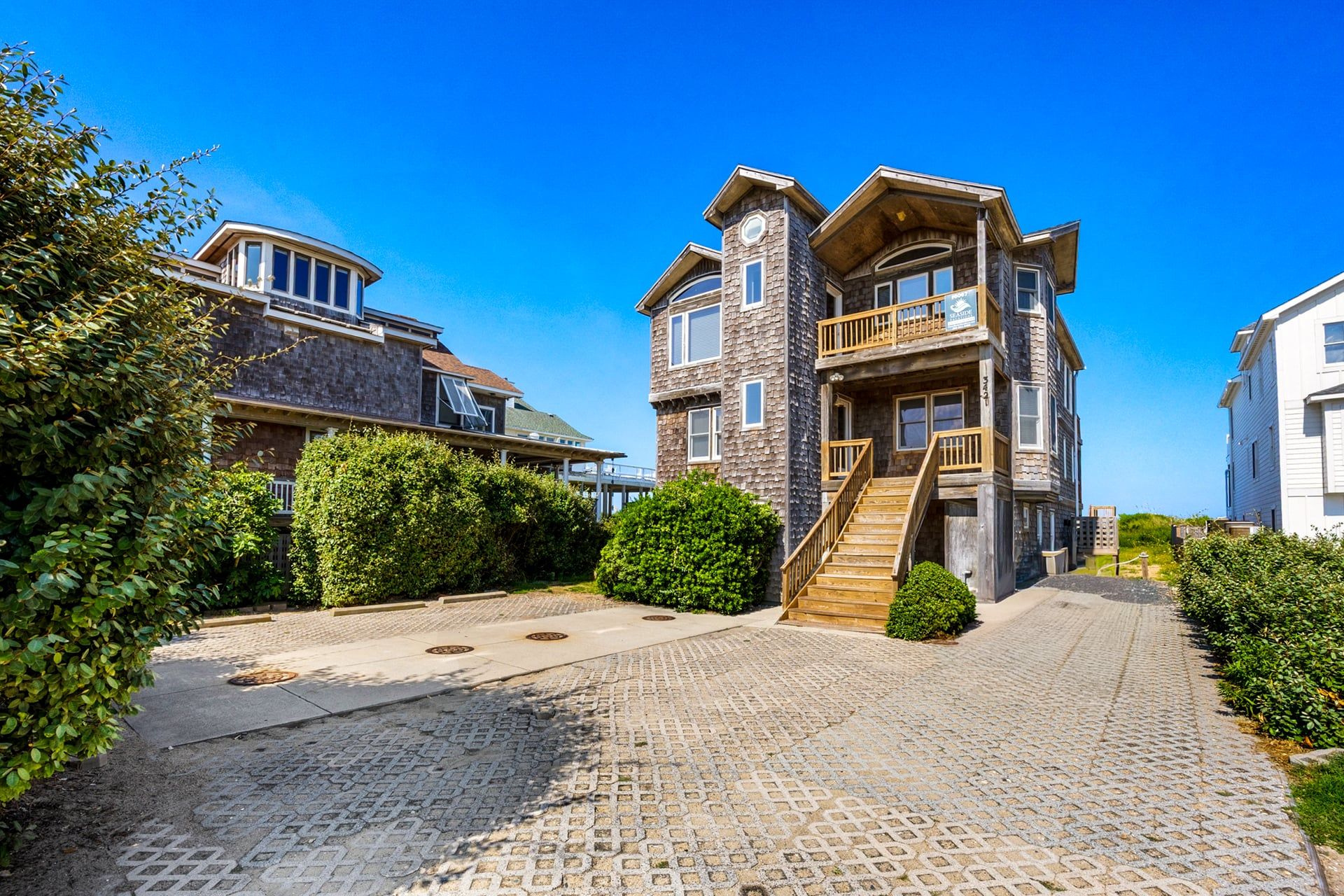 A two-story house with a stone facade, a wooden staircase, and a paved driveway.