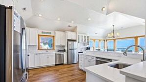 A modern kitchen with white cabinets, stainless steel appliances, and a large island with a sink. - 6120 YankeeClipper*Oceanfront*Elevator*Pool*HotTub (Nags Head)