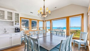 A spacious dining area with a view of the ocean, wooden flooring, and a chandelier. - 6120 YankeeClipper*Oceanfront*Elevator*Pool*HotTub (Nags Head)