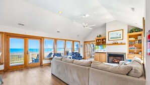 A spacious living room with a large sectional sofa, a fireplace, a television, and a bookshelf. - 6120 YankeeClipper*Oceanfront*Elevator*Pool*HotTub (Nags Head)