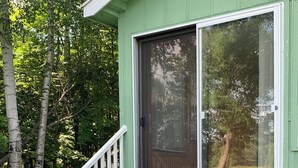 Eine Holztreppe führt zu einem grünen Gebäude mit einem großen Fenster und einem weißen Geländer.