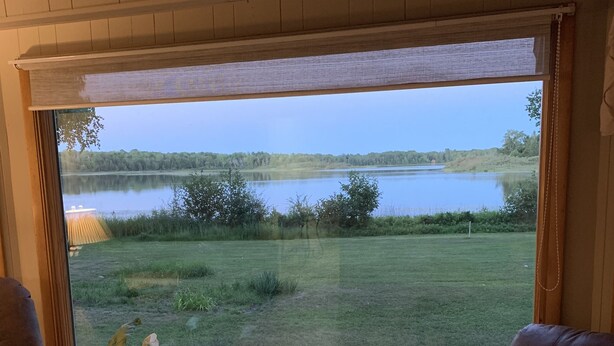 Ein Zimmer mit großem Fenster mit Seeblick, zwei Ledersessel, Holzboden und ein Blumentopf.