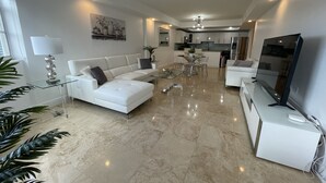 Una sala de estar moderna con un sofá blanco, una mesa de centro de vidrio y un televisor de pantalla plana.