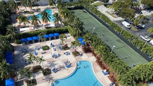 Un resort con una amplia piscina, canchas de tenis y zonas de descanso a la sombra.