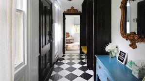 A hallway with a black and white checkered floor, a blue console table, and a large ornate mirror. - Locktender Cottage · Historic cottage near Mohonk & Minnewaska, 2BR/2BA (High Falls)
