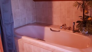 Un baño con bañera, paredes de azulejos y una planta en maceta.