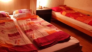 Una habitación con dos camas individuales, cada una con cabecero de madera, una mesita de noche con lámpara y un estante en la pared con velas.