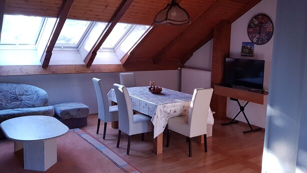 Acogedor cuarto ático con una mesa de comedor, sillas, un sofá y una televisión.