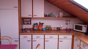 Una cocina compacta con armarios blancos, una encimera de madera y un microondas. Hay varios alimentos y utensilios de cocina sobre la encimera.