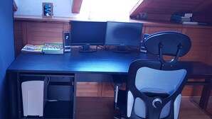 Un escritorio de madera con dos monitores, una silla y un altavoz.