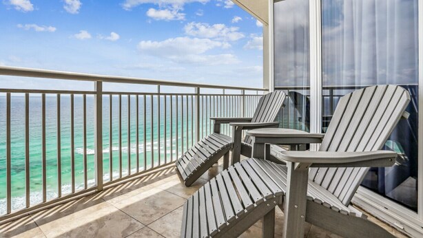 A balcony with a view of the ocean, featuring two Adirondack chairs and a glass door. - Neaux Worries: Newly remodeled Ocean Front 16th Floor Pearl Condo! (Navarre Beach)