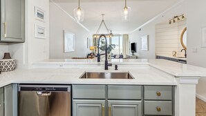 A modern kitchen with a central island, stainless steel dishwasher, and a large mirror above the sink. - Neaux Worries: Newly remodeled Ocean Front 16th Floor Pearl Condo! (Navarre Beach)