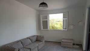 A room with a wicker sofa, a small ottoman, a window with shutters, and a hanging light fixture. - Magnifique Villa Neuve Avec Piscine (Le Marin)