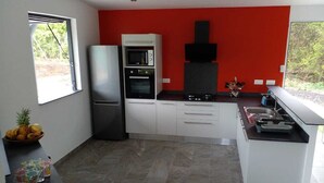 A modern kitchen with white cabinets, a red accent wall, a built-in oven, and a microwave. - Magnifique Villa Neuve Avec Piscine (Le Marin)
