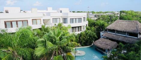 A resort with a swimming pool surrounded by lush greenery and thatched-roof structures.