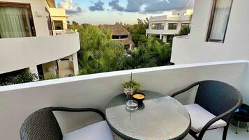A balcony with two wicker chairs and a small round table, overlooking a residential area with modern houses and lush greenery.
