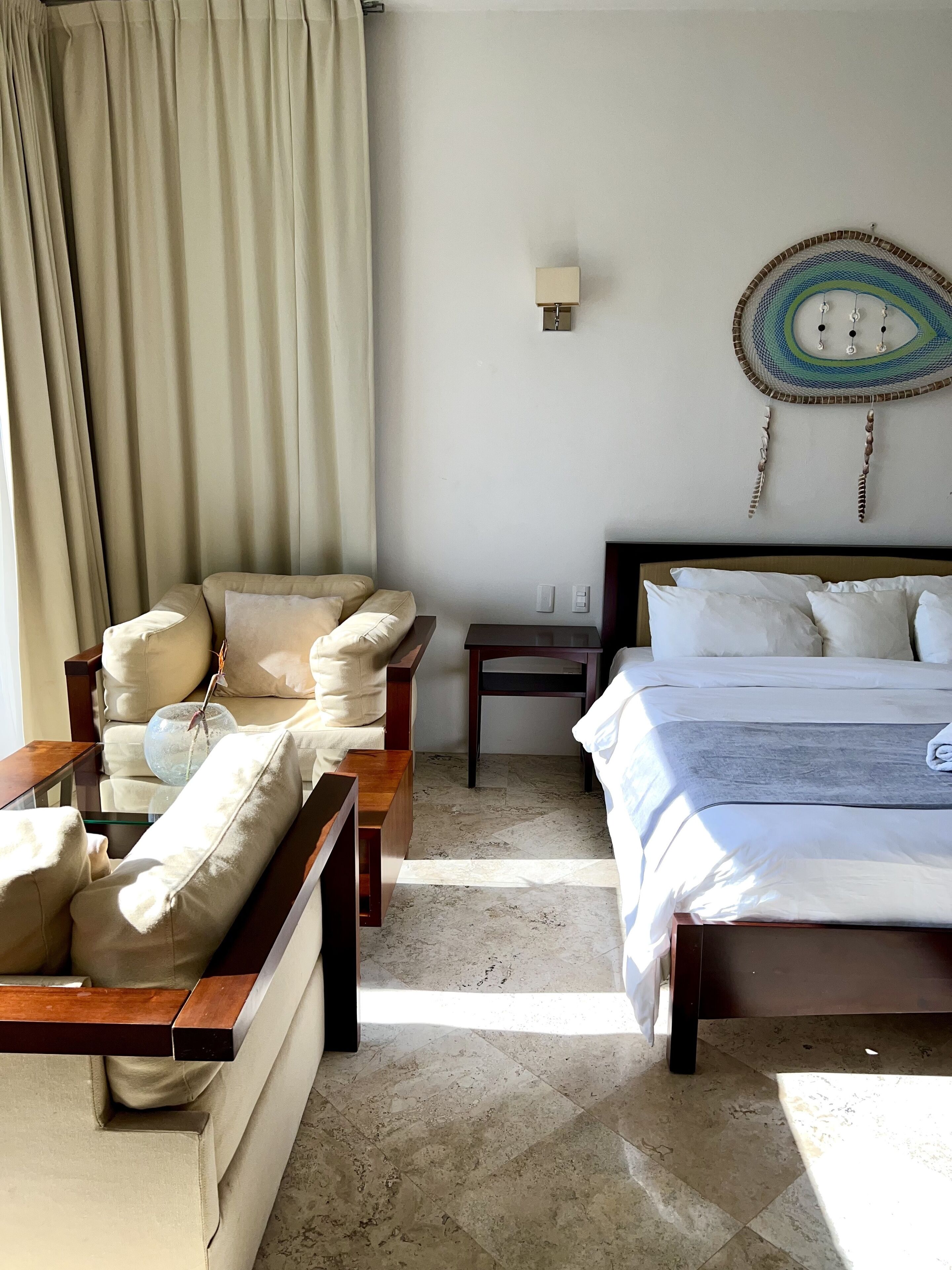 A hotel room with a bed, a sofa, a small table, and a wall-mounted lamp.