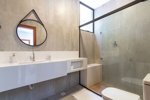 A modern bathroom with a large mirror, a white vanity, a glass shower enclosure, and a toilet.