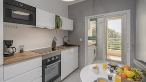 A modern kitchen with white cabinetry, a wooden countertop, and a built-in oven. There is a window with a view of greenery outside.